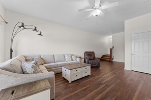 Ein Wohnzimmer mit einer Eckcouch, einem Couchtisch, einem Sessel, einer Stehlampe und einem Deckenventilator.