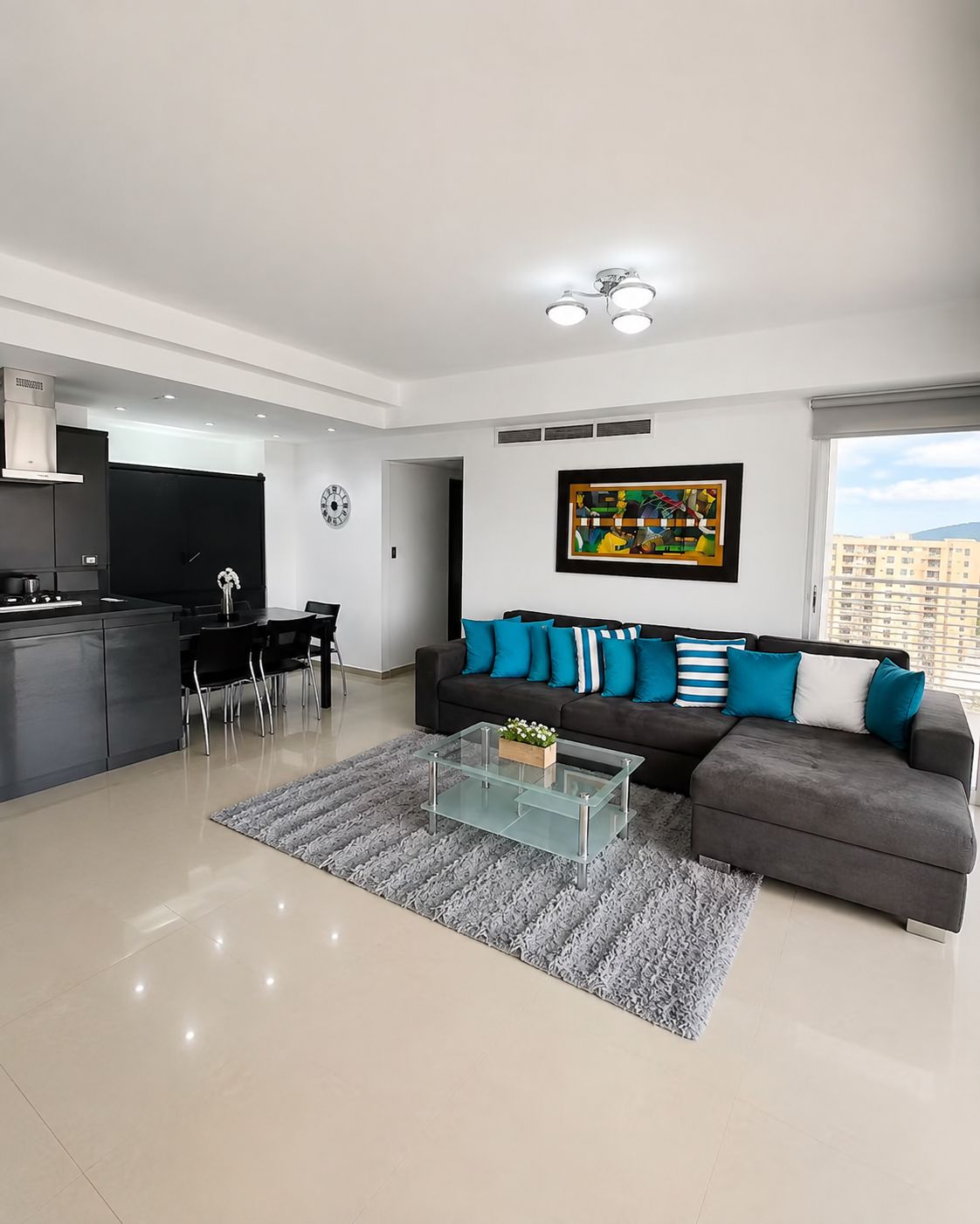 A modern living room with a grey sofa, a glass coffee table, and a dining area with chairs.