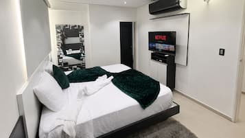 A modern bedroom with a bed, a flat-screen TV mounted on the wall, and a built-in air conditioning unit.