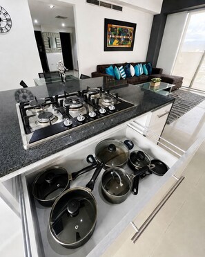 A modern kitchen with a built-in gas stove, a glass-top island, and a variety of cookware stored underneath. - Lujo&Exclusividad, Bello Apto con Planta Eléctrica (Barquisimeto)