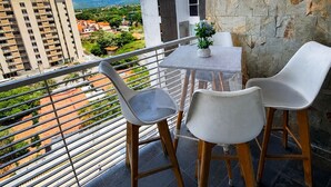 En balkon med et bord og stole, der udover en byudsigt med bygninger og grønne områder.