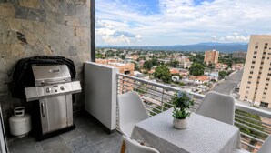 En balkon med grill, et bord med stole og udsigt over bybilledet.