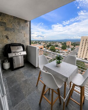 A balcony with a grill, a table with chairs, and a view of a cityscape. - Lujo&Exclusividad, Bello Apto con Planta Eléctrica (Barquisimeto)