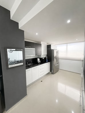 A modern kitchen with a stove, sink, and refrigerator, featuring a minimalist design and ample natural light.