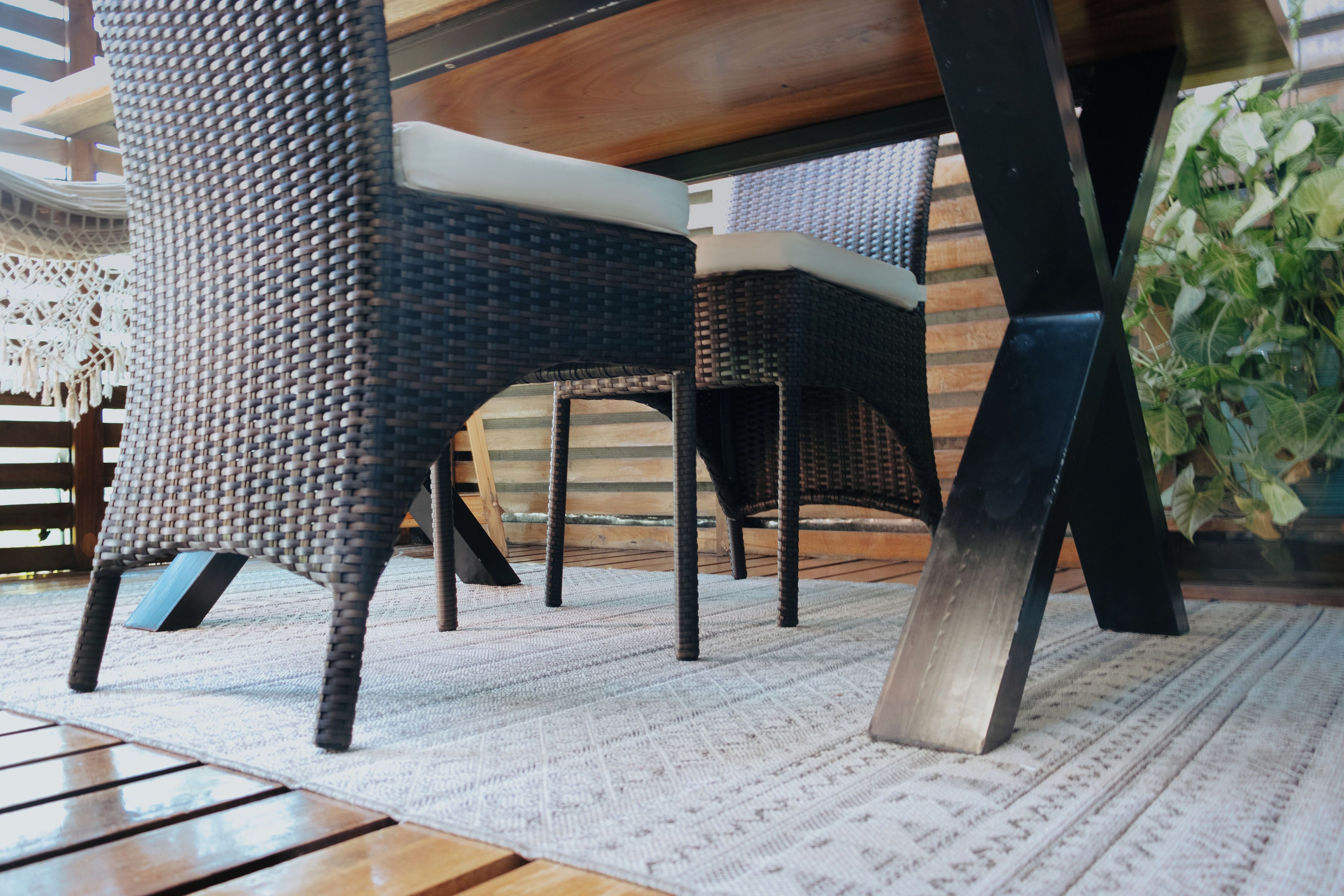 A dining area with wicker chairs, a wooden table, and a patterned rug.