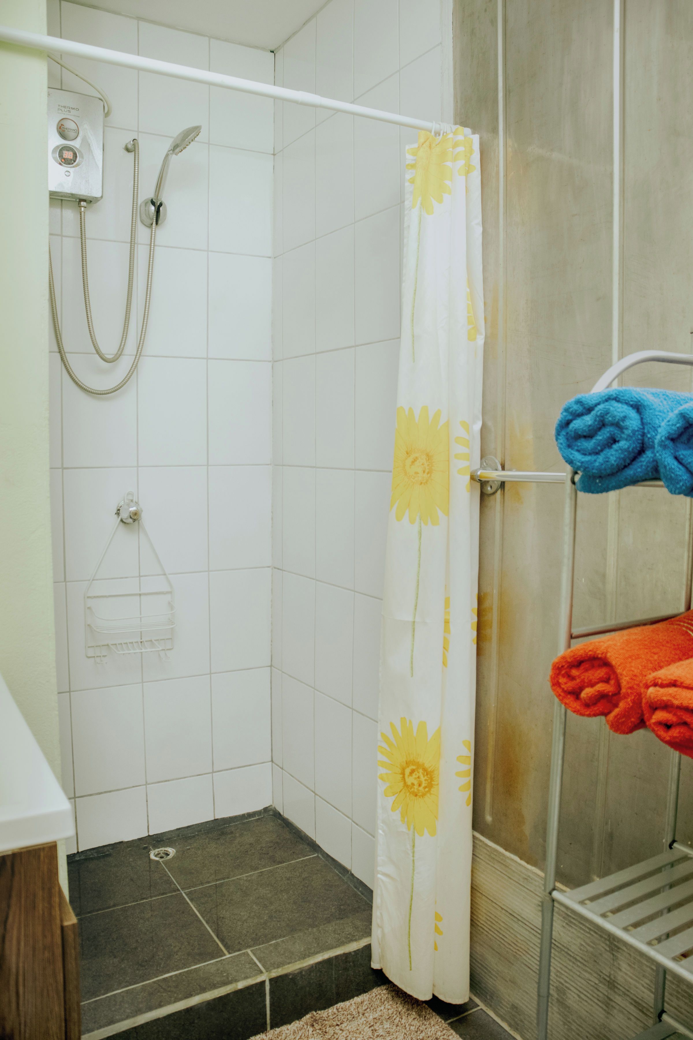A shower area with a white shower curtain featuring yellow floral patterns, a handheld showerhead, and a wall-mounted control panel.