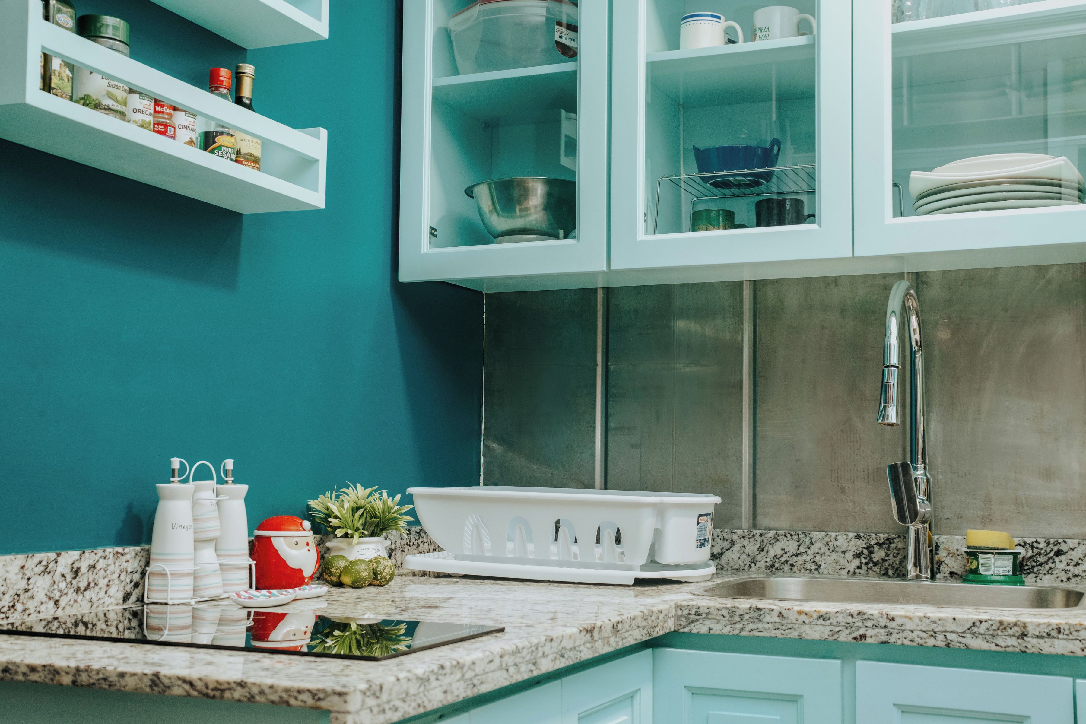 A kitchen with teal cabinets, a stainless steel sink, and various kitchen items on the counter.