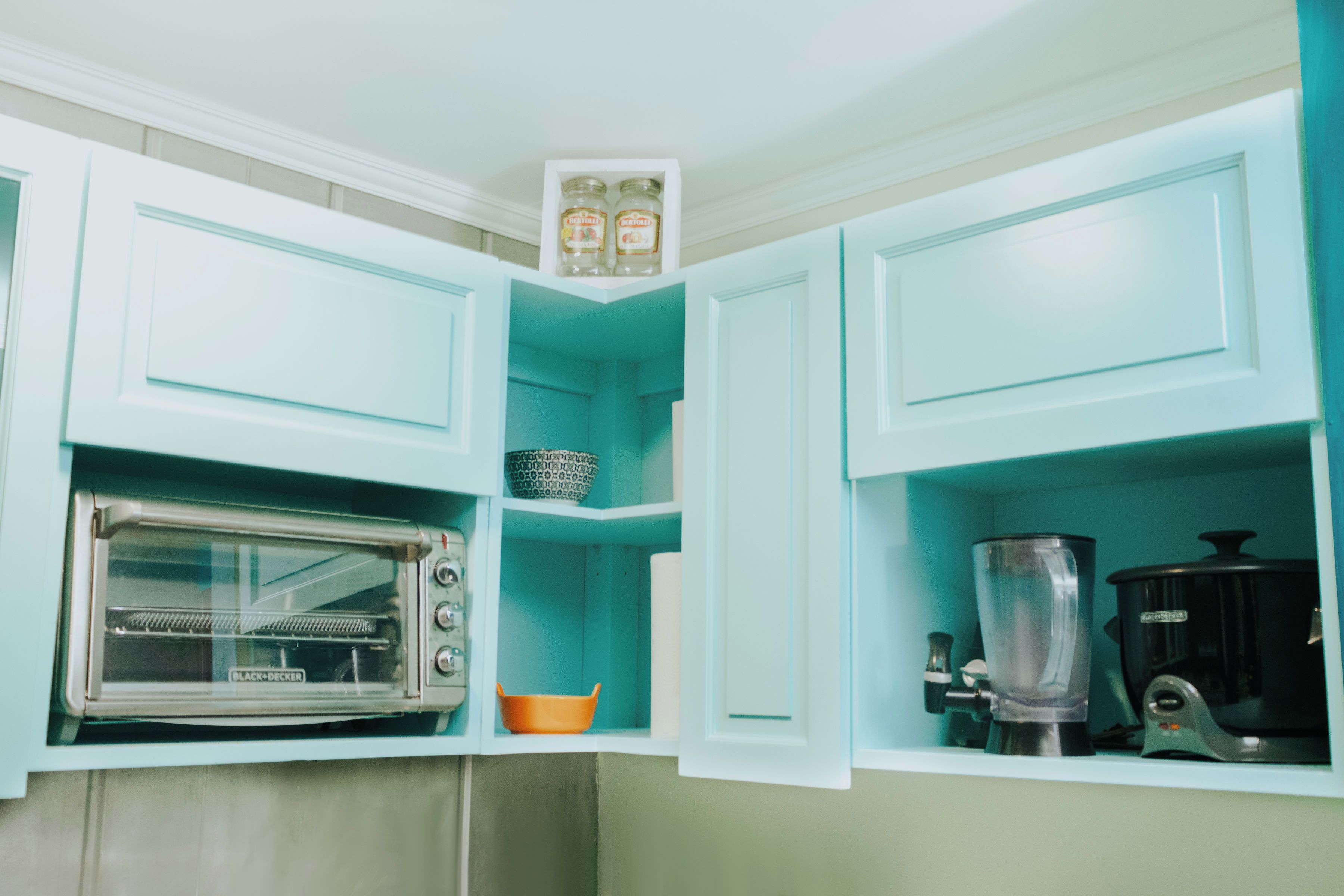 Een keuken met blauwgroene kastjes, een zwarte koffiezetapparaat en een elektrische oven.