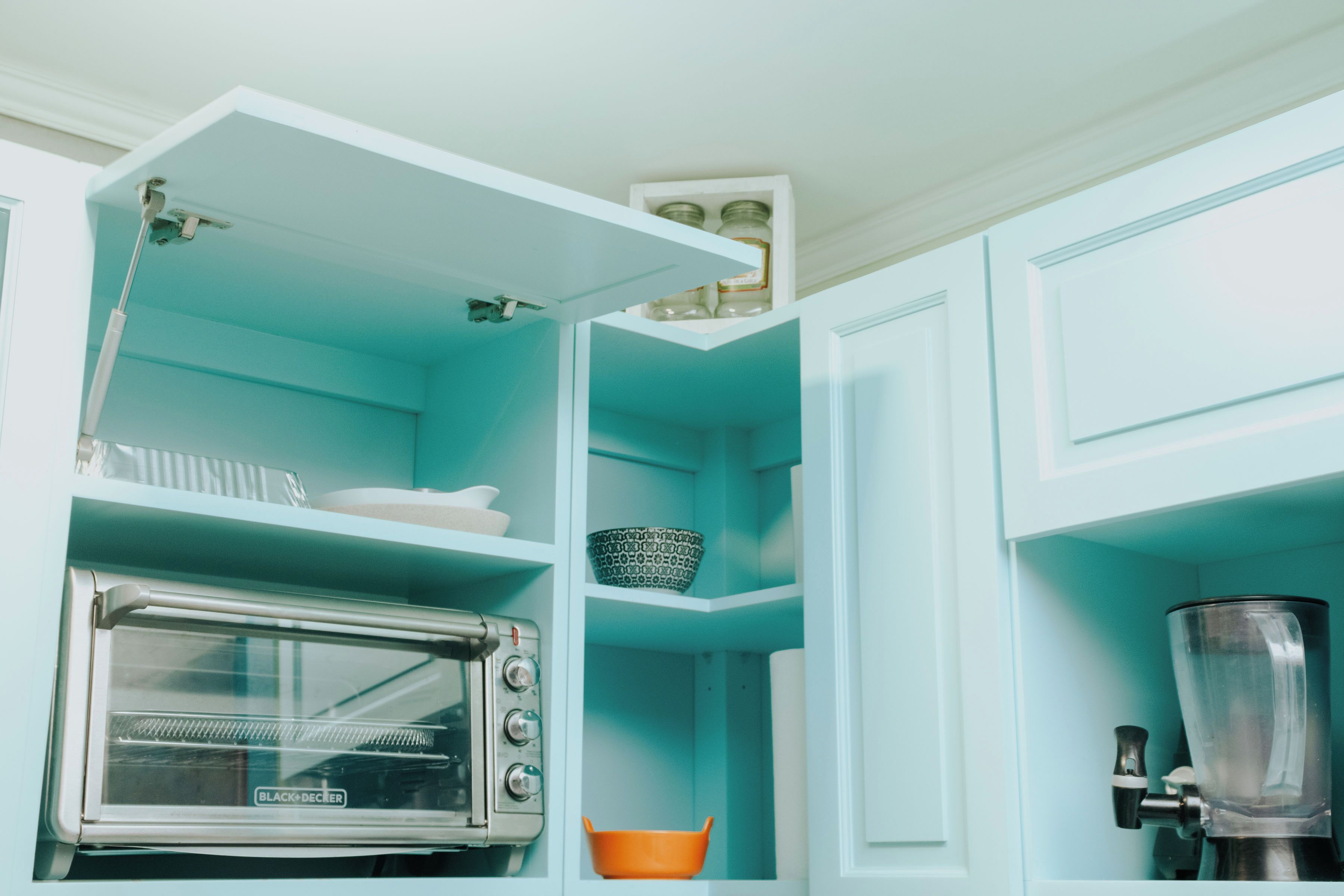 A kitchen with a built-in toaster oven, a blender, and shelves with dishes and jars.