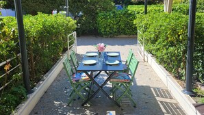 Ein Essbereich im Freien mit einem Tisch für vier Personen, umgeben von grünen Stühlen und einem Blumenstrauß.