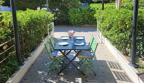 Ein Essbereich im Freien mit einem Tisch für vier Personen, umgeben von grünen Stühlen und einem Blumenstrauß.