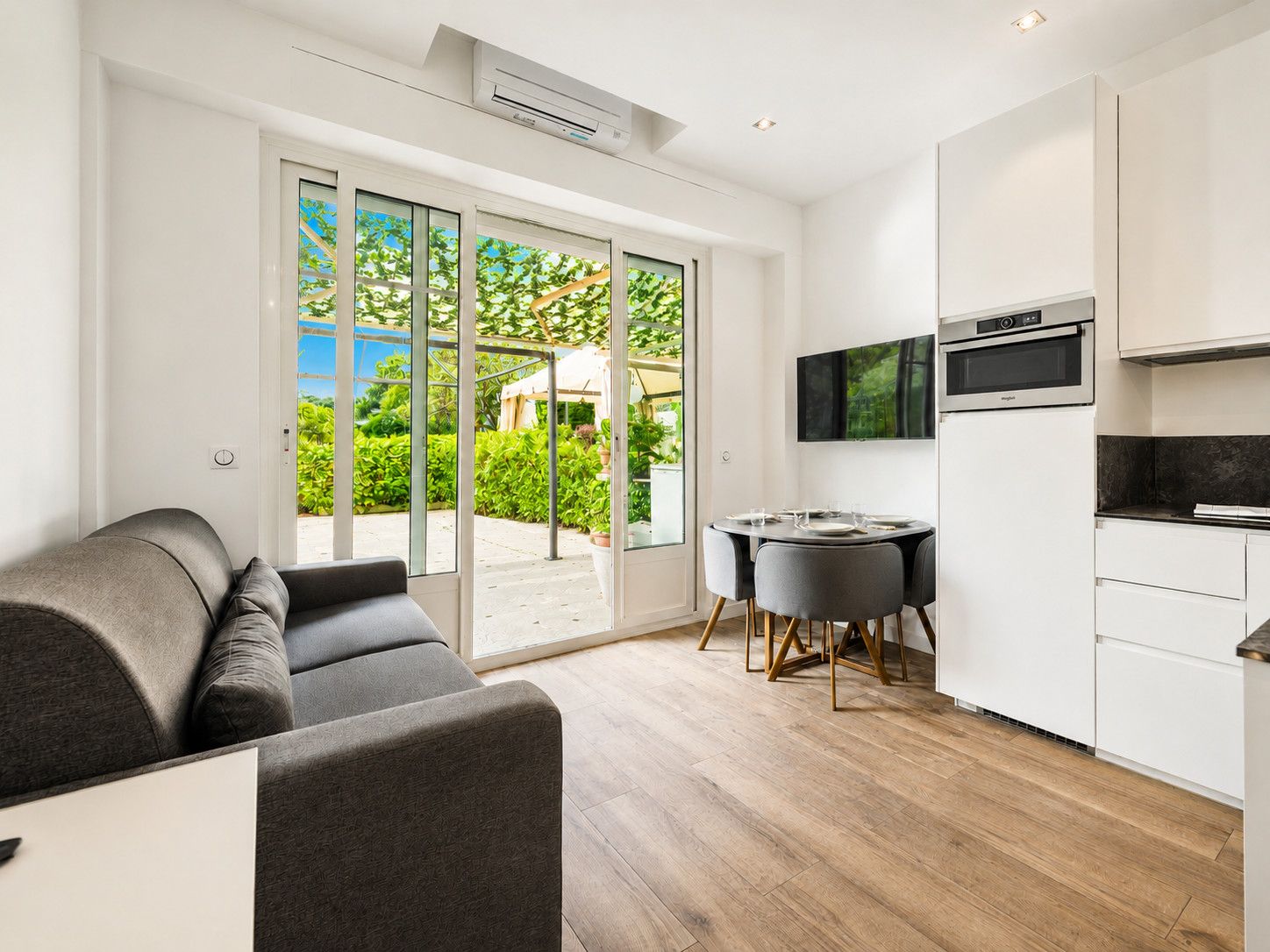 A modern kitchen with a dining area, a sofa, and a sliding glass door leading to a garden.