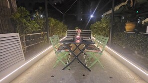 Ein Sitzbereich im Freien mit Tisch und Stühlen, umgeben von Pflanzen und einem Zaun.