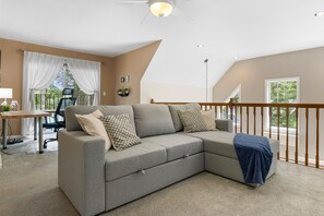 Ein modernes Wohnzimmer mit einem grauen Ecksofa, einem Holzbalkon und Blick ins Freie.