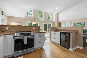 A modern kitchen with a built-in oven, a refrigerator, and a dishwasher. There is a dining area with a table and chairs visible through the glass doors. - Laurel Shores | 3BR/3BA Oceanfront Harpswell Retreat w/ Deck (Harpswell)