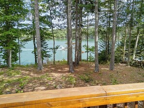 A wooden deck overlooking a lake with trees and a dock. - Laurel Shores | 3BR/3BA Oceanfront Harpswell Retreat w/ Deck (Harpswell)