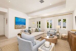 Un salon moderne avec un canapé, des fauteuils, une table basse et un tableau représentant une scène de plage.