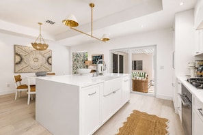 A modern kitchen with a central island, white cabinetry, and a dining area with chairs. - New! 1 Palm - Exclusive Palm Beach Luxe Escape (West Palm Beach)