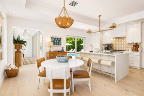 A modern kitchen with white cabinetry, a central island, and a dining area with white chairs. - New! 1 Palm - Exclusive Palm Beach Luxe Escape (West Palm Beach)