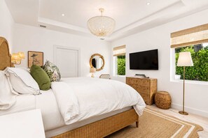 A bedroom with a bed, a dresser, a television, a mirror, and a window with a view of greenery. - New! 1 Palm - Exclusive Palm Beach Luxe Escape (West Palm Beach)