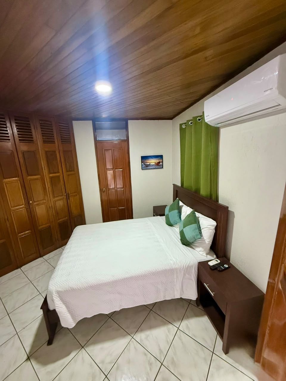 A bedroom with a bed, wooden wardrobe, a nightstand, and an air conditioning unit.