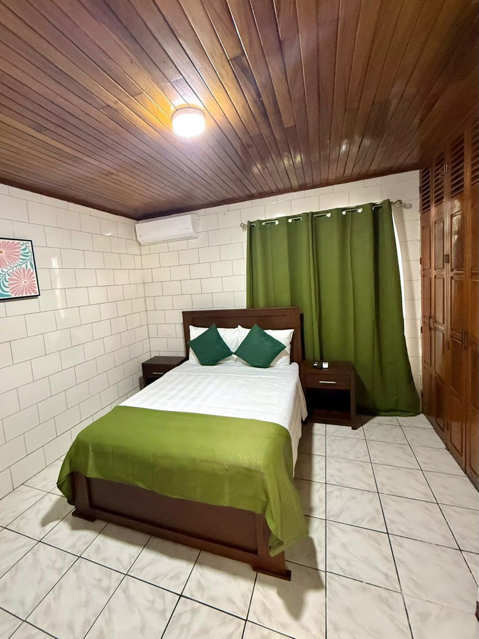 A room with a bed, a nightstand, a wooden ceiling, and a green curtain.
