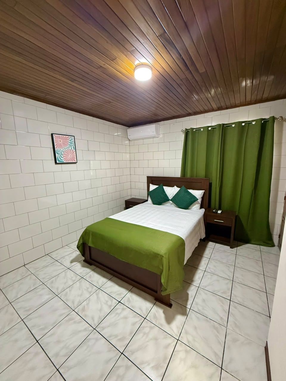 A room with a bed, a nightstand, a green curtain, and a wall-mounted air conditioner.
