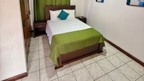 A bedroom with a wooden ceiling, a bed with a green bedspread, a nightstand, a wall-mounted air conditioner, and two framed pictures on the wall.