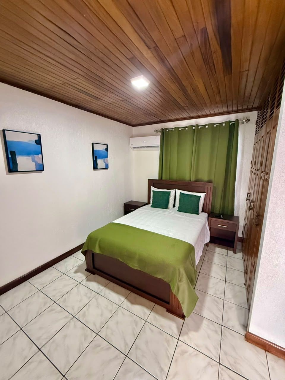 Un dormitorio con cama, mesita de noche, aire acondicionado en la pared y cortina verde.