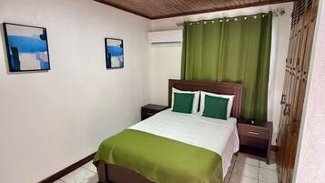 Un dormitorio con cama, mesita de noche, aire acondicionado en la pared y cortina verde.