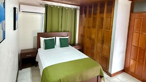 A bedroom with a wooden ceiling, a bed with green bedding, a wardrobe, and a nightstand.