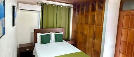 A bedroom with a wooden ceiling, a bed with green bedding, a wardrobe, and a nightstand.