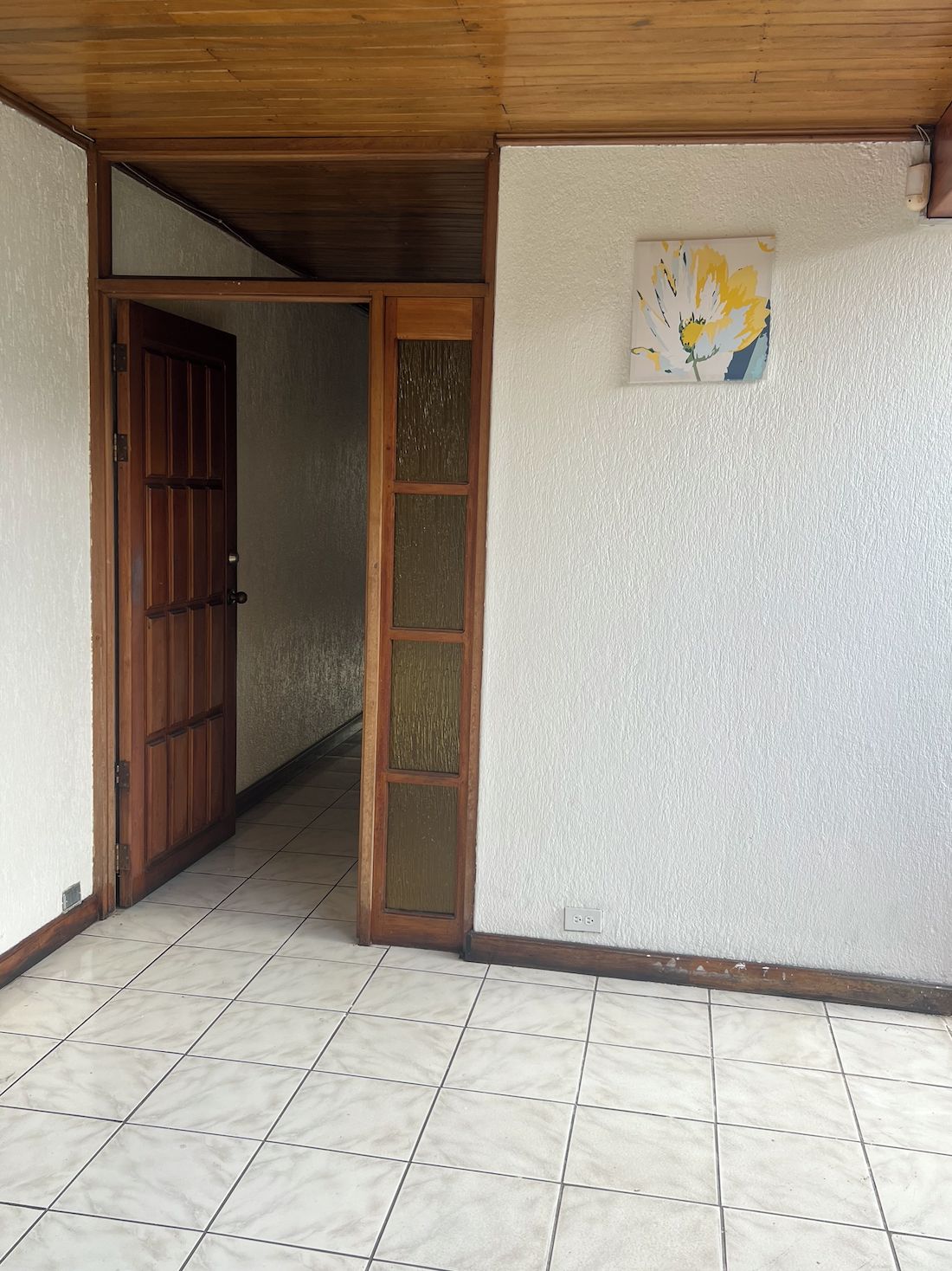 Una habitación con puerta de madera, puerta de vidrio y una lámpara fijada a la pared.