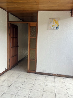 Una habitación con puerta de madera, puerta de vidrio y una lámpara fijada a la pared.