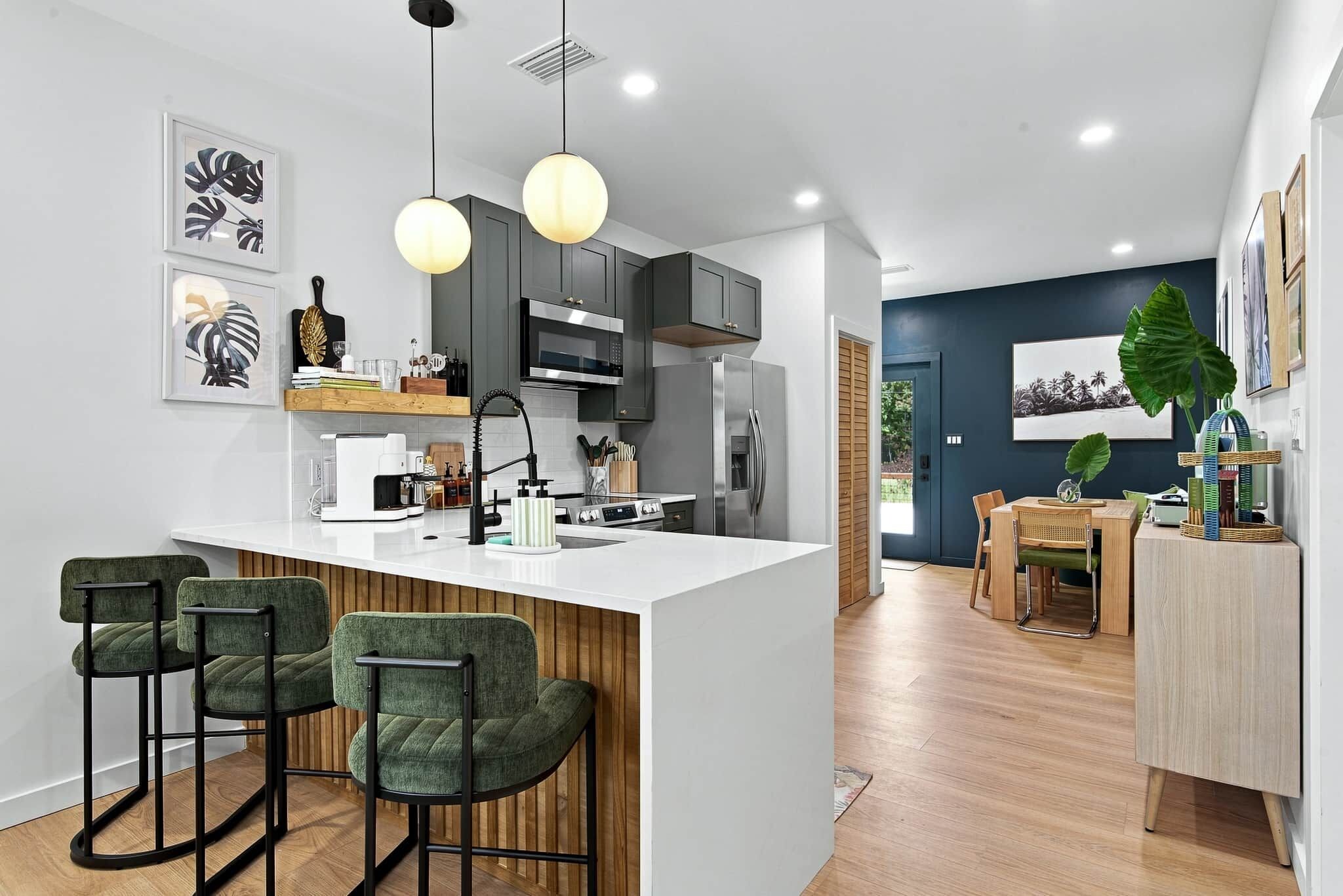 A modern kitchen with a central island, bar stools, and a dining area with a table and chairs.