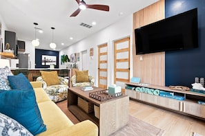 A modern living room with a sofa, coffee table, and a TV mounted on the wall. - Modern Hideaway · Hot Tub · Golf Cart · Kayaks (Walton County)