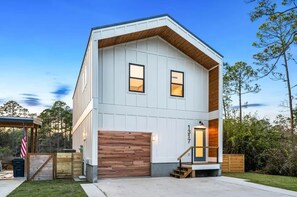 A modern two-story house with a garage, a wooden deck, and a well-maintained lawn. - Modern Hideaway · Hot Tub · Golf Cart · Kayaks (Walton County)