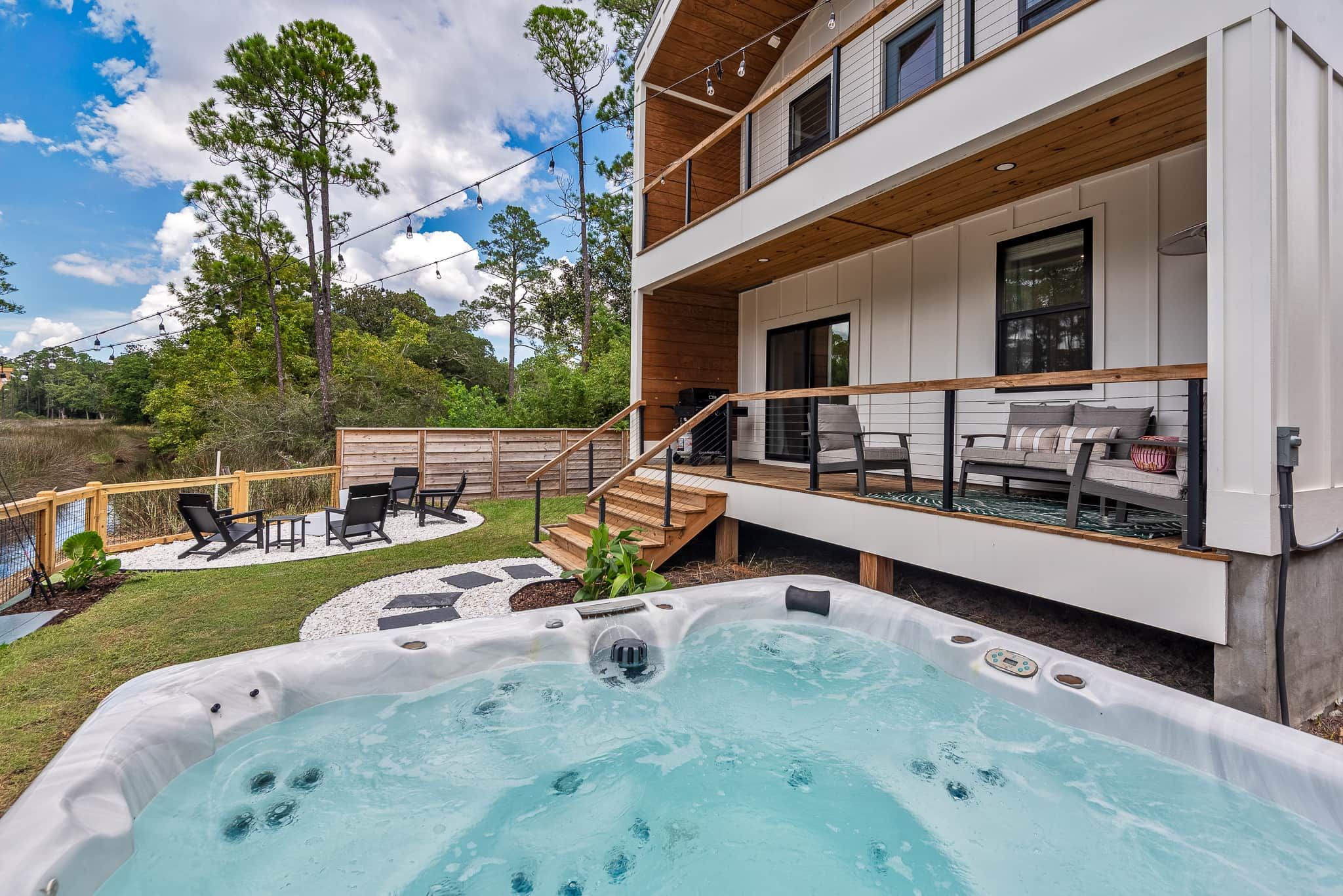 A modern two-story house with a hot tub, outdoor seating, and a deck.