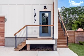 A modern two-story house with a blue door, a wooden staircase, and a number '1317' on the wall. - Modern Hideaway · Hot Tub · Golf Cart · Kayaks (Walton County)