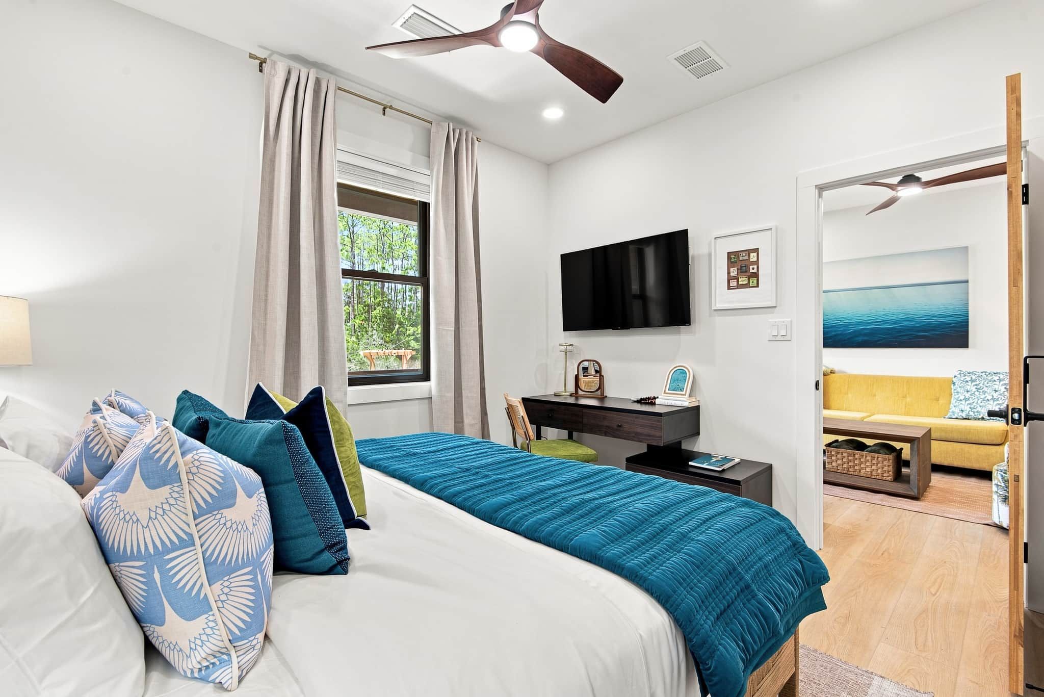 A modern bedroom with a large bed, a desk, a TV, and a view of the outdoors.