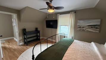 Een slaapkamer met een bed, een plafondventilator, een televisie, een bureau en een raam met gordijnen.