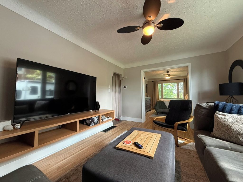 A living room with a flat-screen TV, wooden entertainment unit, and a ceiling fan.