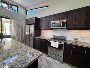 A modern kitchen with dark cabinetry, a stainless steel refrigerator, a microwave, and a gas stove. - Tropical Escape 3 BR Private Pool / lawn / Fenced (Sosua)