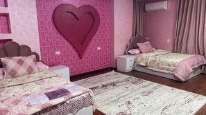 A bedroom with two beds, a large heart-shaped decoration on the wall, and a bedside table with a lamp.
