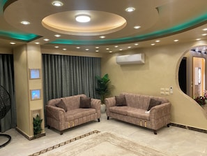 A living room with two sofas, a ceiling with recessed lighting, an air conditioning unit, and a large mirror. - Near the pyramids and the new Grand Egyptian Museum! (Pyramids garden)