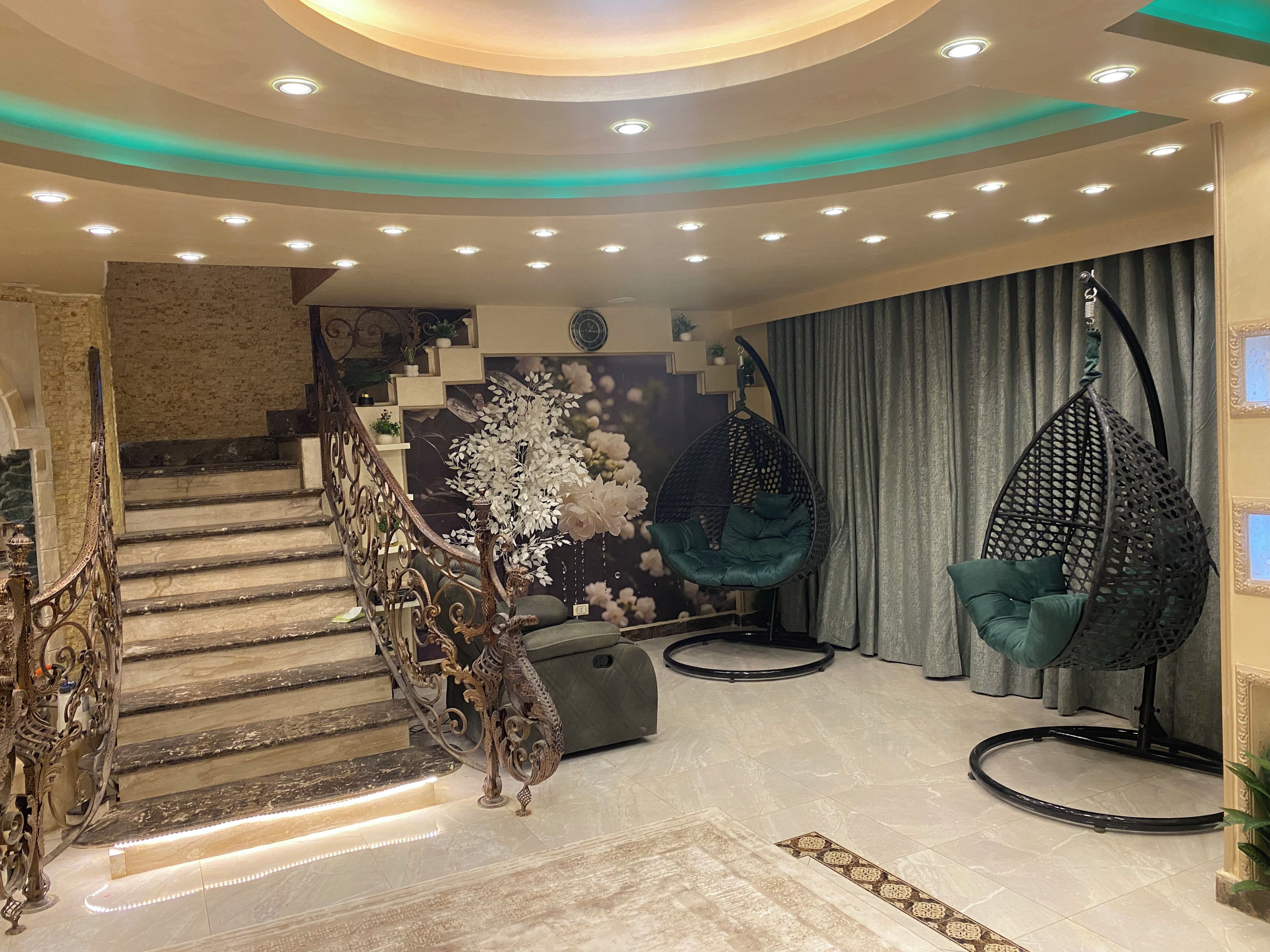 A modern interior with a staircase, decorative wall, hanging chairs, and a patterned rug.