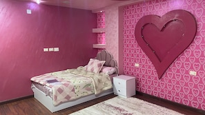 Ein Schlafzimmer mit einem Bett, einem Nachttisch, einem Wandregal und einer großen herzförmigen Dekoration.