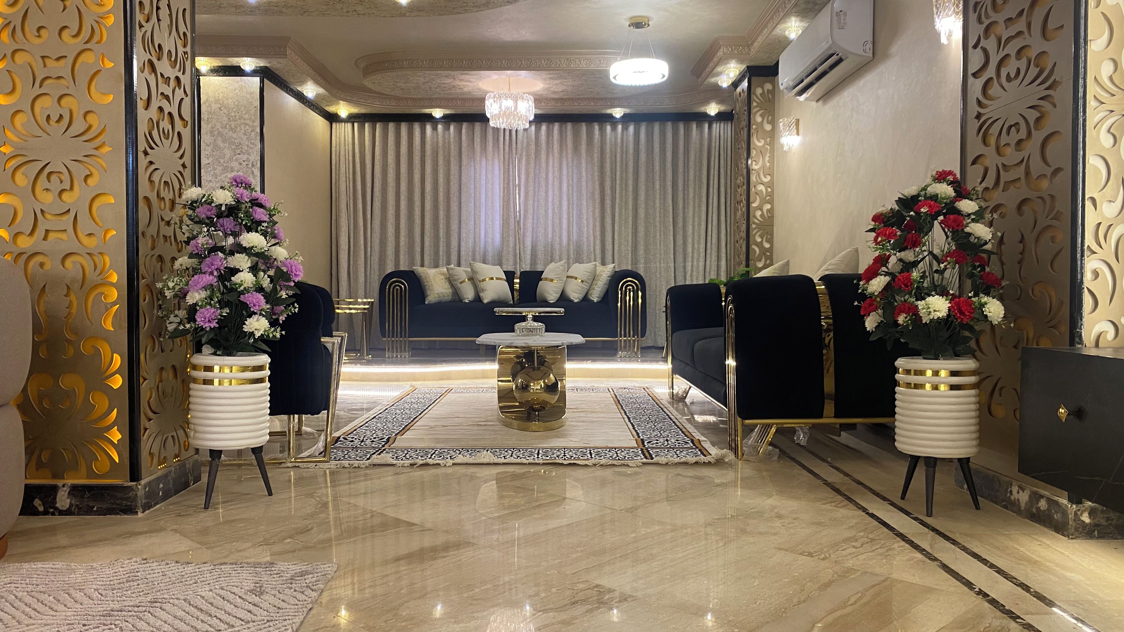 A luxurious living room with a marble floor, a central coffee table, a sofa set, and decorative vases with flowers.