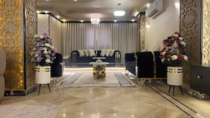 Ein luxuriöses Wohnzimmer mit Marmorboden, einem zentralen Couchtisch, einer Sofagarnitur und dekorativen Vasen mit Blumen.