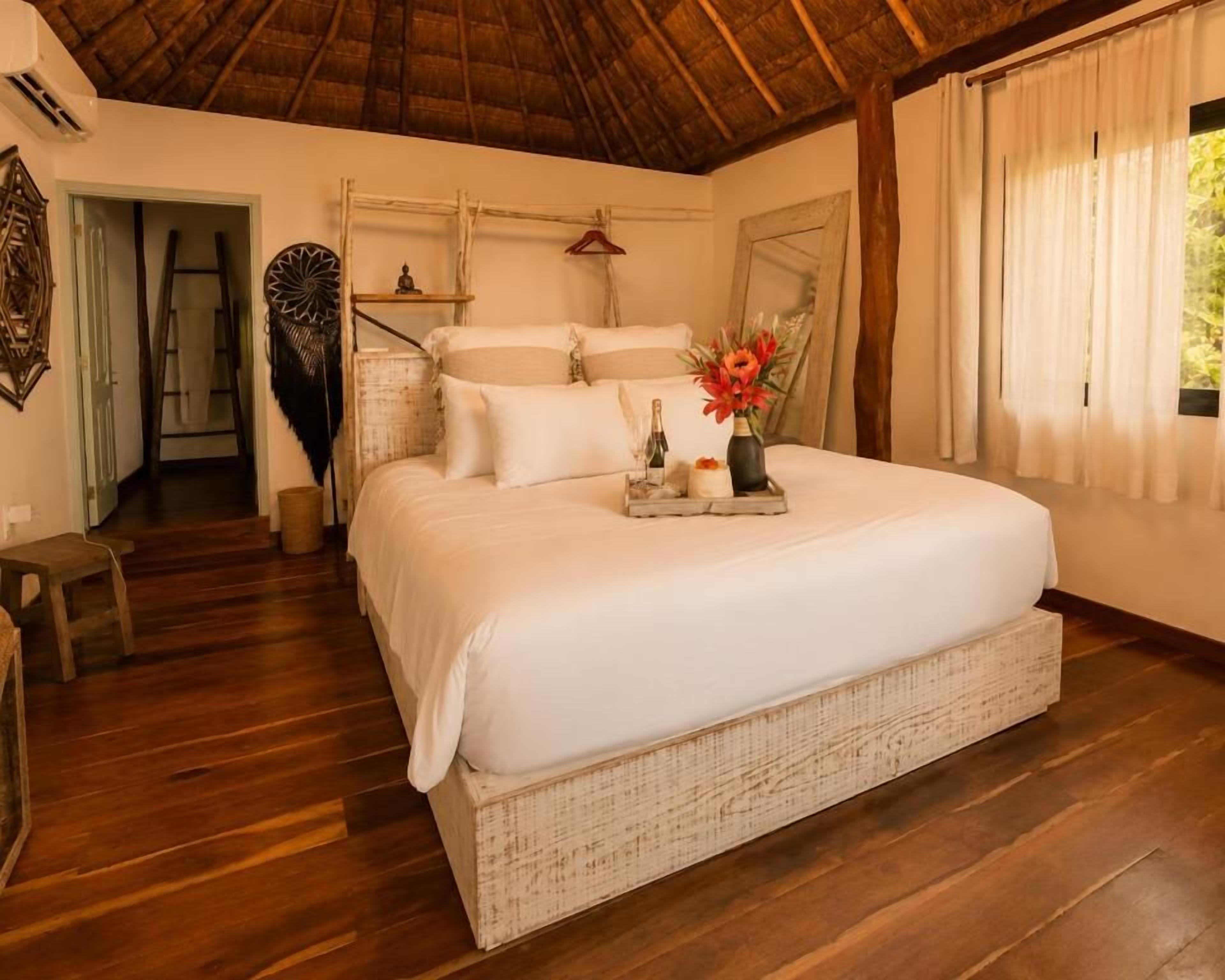 Quarto espaçoso com uma cama grande, piso de madeira e teto de palha.